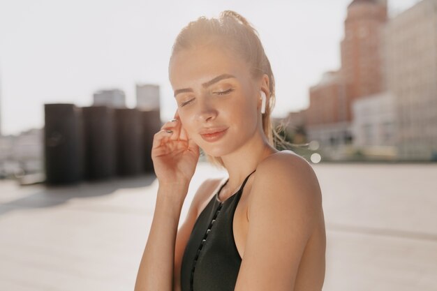 Close up portrait of pretty charming lady engaged in sports exercises and listening music in sunlight in the city. Sport, exercise