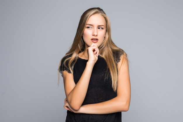 Close up portrait of pretty confident thoughtful girl, holding hand near the face, looking seriously up, standing over grey background with copy space