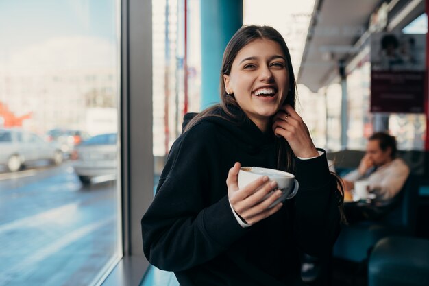 Close up portrait of pretty female drinking coffee. Lady holding a white mug with hand.