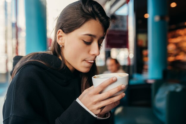 Close up portrait of pretty female drinking coffee. Lady holding a white mug with hand.