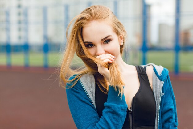 Close-up portrait of a pretty girl standing on the stadium.She wears blue jacket and black shirt. She is looking to the camera.