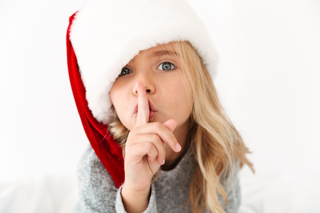 免费照片特写肖像漂亮的小女孩在圣诞老人的帽子显示沉默的姿态，