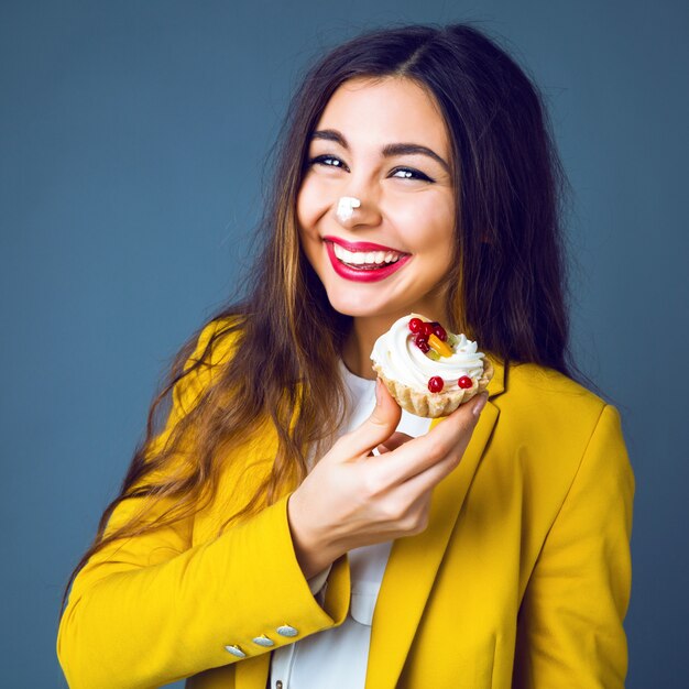 Close up portrait of pretty young brunette woman with bright makeup eating tasty cake with berries and cream.