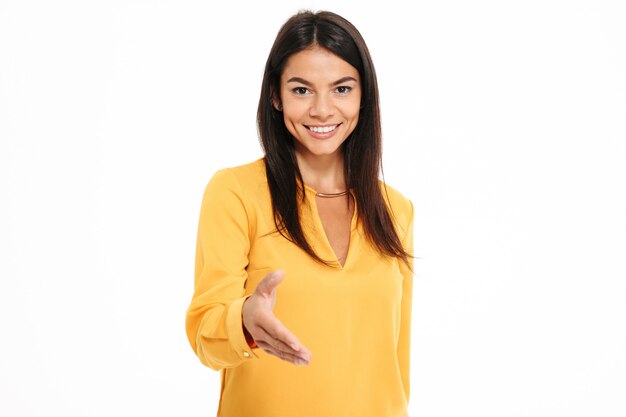 Close-up portrait of pretty young woman in yellow shirt holding out her hand to greet someone