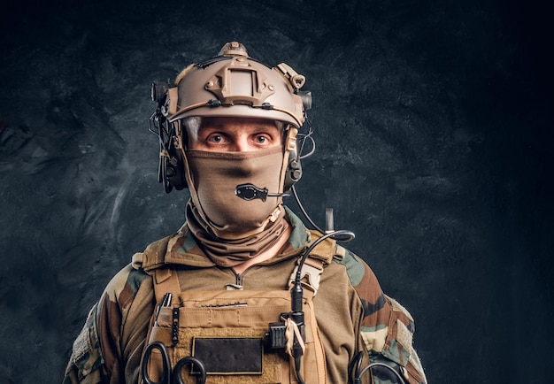 Close-up portrait. Private security service contractor in camouflage helmet with walkie-talkie. Studio photo against a dark textured wall