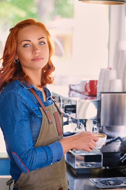 Close up portrait of redhead female barista drinks coffee.