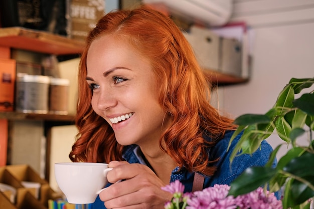 Close up portrait of redhead female barista drinks coffee.