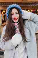 Free photo close-up portrait of romantic european girl with dark hair posing with sweet christmas lollipop. photo of pretty caucasian female model in white gloves and blue hat having fun