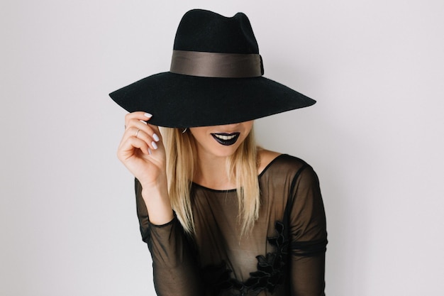 Free photo close up portrait of romantic woman with dark lips and wonderful smile is covering face by hat and holding hat over isolated background