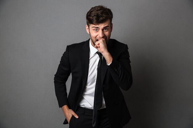 Close-up portrait of scared man in black suit bites his fist, 