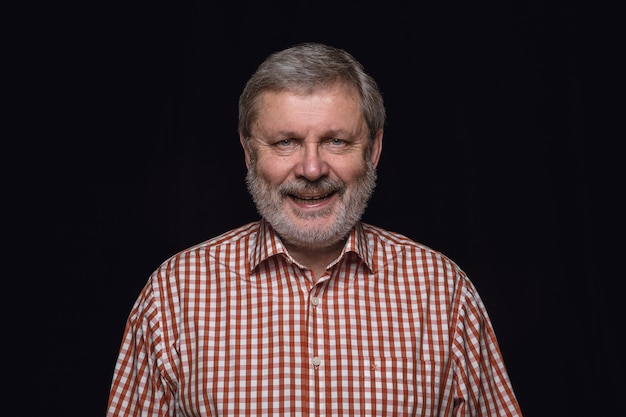 Close up portrait of senior man isolated on black studio background. Smiling, feeling happy.