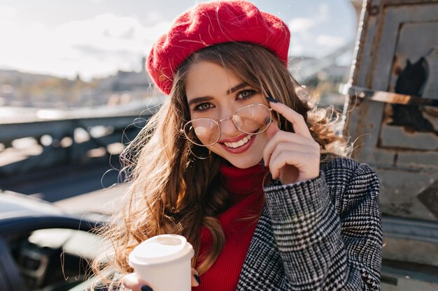 Close-up portrait of sensual brown-haired woman with cup of hot beverage posing in cold day