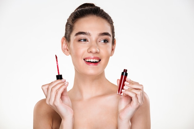 Close up portrait of sensual brunette woman with hair in bun applying lip gloss being satisfied