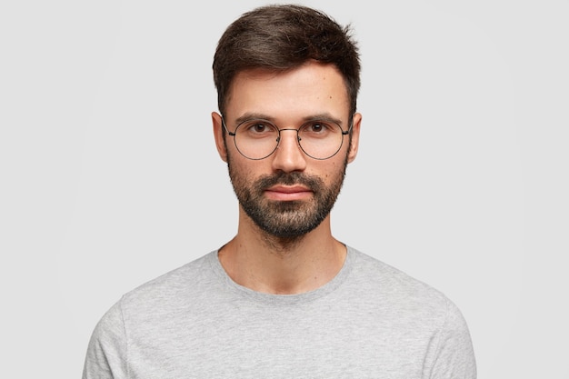 Close up portrait of serious attractive man student with dark bristle, wears spectacles