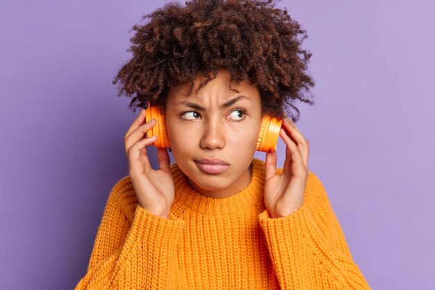 深刻な若いアフリカ系アメリカ人女性のクローズアップの肖像画は、ワイヤレスヘッドフォンのポーズを着てどこかに集中したオーディオトラックを聞きます