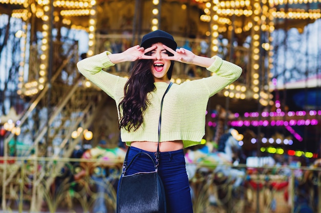 Free photo close up portrait of sexy  fancy stylish woman have fun and smile on attractions. wearing trendy hipster swag black hat and neon  sweater .