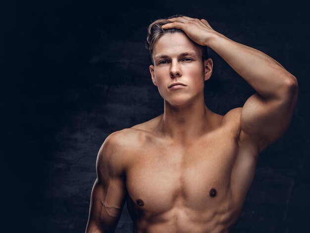 Close-up portrait of a sexy shirtless young man model with a muscular body and stylish haircut posing at a studio. Isolated on a dark background.