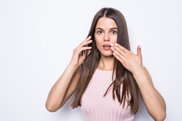 Close up portrait of shocked woman talking to somebody on the phone on white wall.