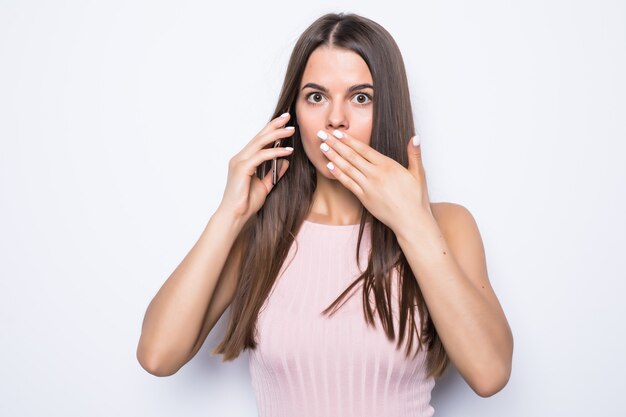 Close up portrait of shocked woman talking to somebody on the phone on white wall.