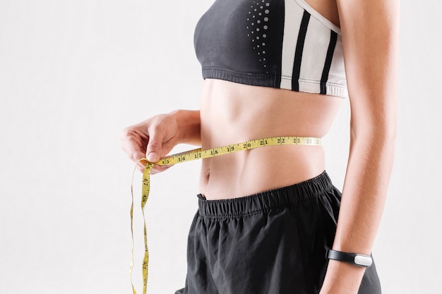 Close up portrait of a slim sportswoman measuring her waist