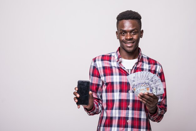 Close up portrait of a smiling african man showing blank screen mobile phone while holding bunch of money banknotes isolated