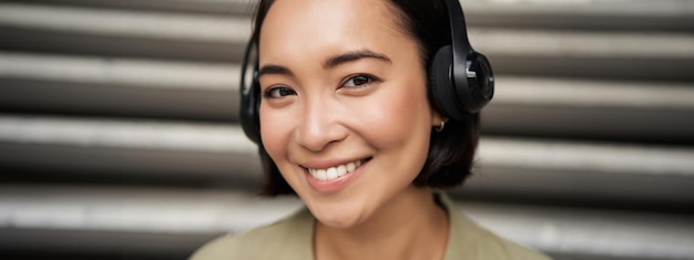 Foto gratuita ritratto ravvicinato di una ragazza asiatica sorridente con le cuffie che ascolta musica all'aperto e sembra felice