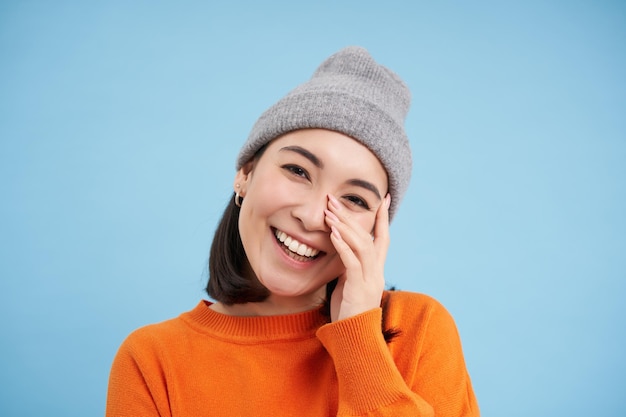 Free photo close up portrait of smiling asian woman in warm hat looking happy and cute at camera has clear natu