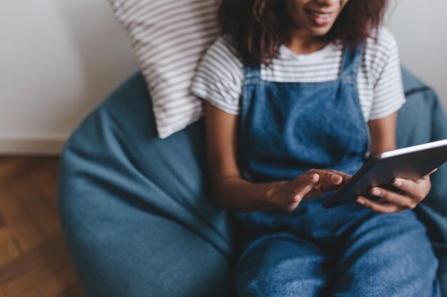 Close-up portrait of smiling black girl in jeans with tablet on foreground