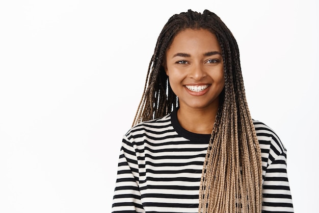 Close up portrait of smiling black girl looking relaxed and happy standing in striped blouse against white background