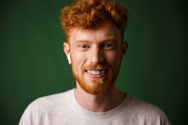 Close-up portrait of smiling curly redhead man, listening to music in airpods