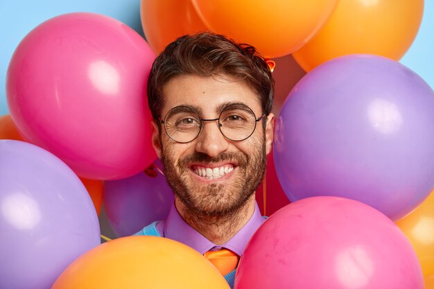 Close up portrait of smiling guy surrounded by party balloons posing