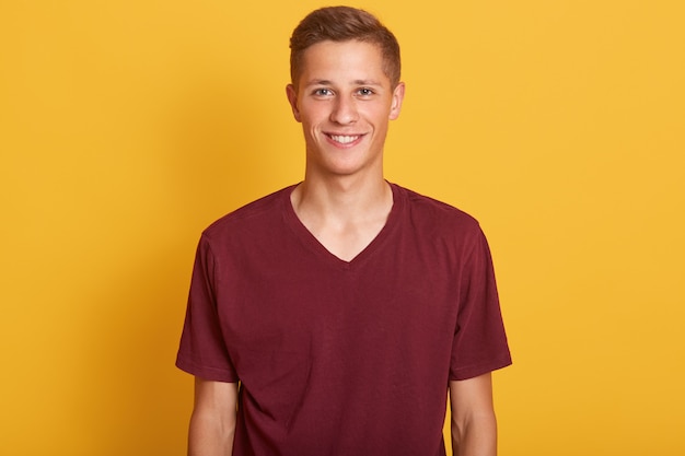 Close up portrait of smiling handsome man with blond hair, wearing in burgunde casual t shirt, standing