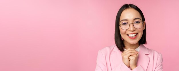 Close up portrait of smiling happy businesswoman in glasses clench hands together thankful excited of smth begging or say please standing over pink background