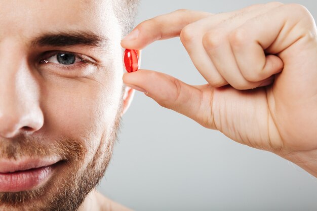 Close up portrait of a smiling man holding red capsule