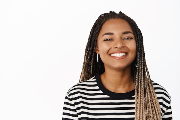 Close up portrait of smiling millennial black girl showing happy face expression cheerful look healthy natural skin and teeth standing over white background