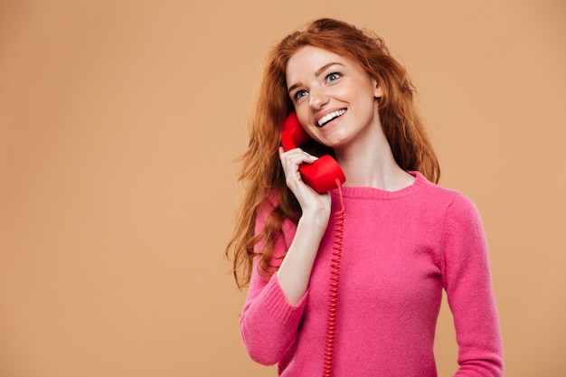 Close up portrait of a smiling pretty redhead girl talking by classic red phone