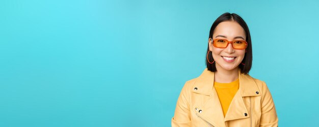 Close up portrait of smiling stylish asian woman in sunglasses looking happy at camera posing in tre