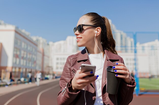 Close-up portrait of smiling woman with long hair, listening to music and drinking coffee