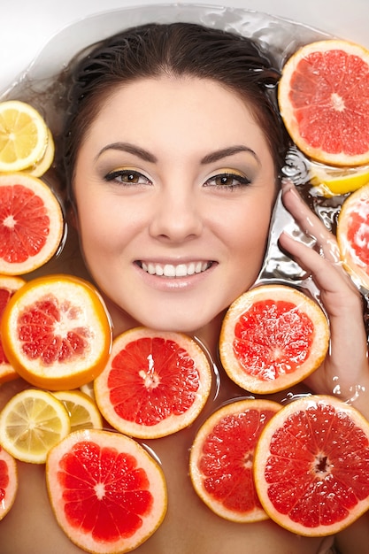 Закройте вверх по портрету усмехаясь женщины с много сочных цитрусовых фруктов грейпфрута лимона в ванной комнате