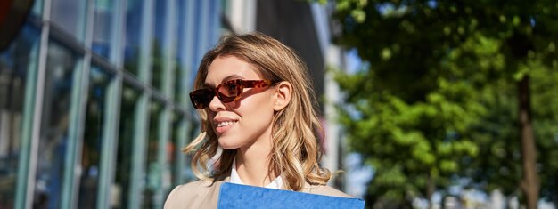 Close up portrait of smiling young woman in sunglasses corporate suit holding a folder with work