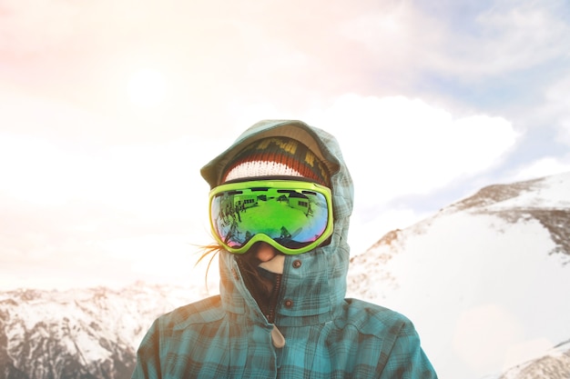 Close up portrait of snowboarder posing in front of sunset and snowy mountains