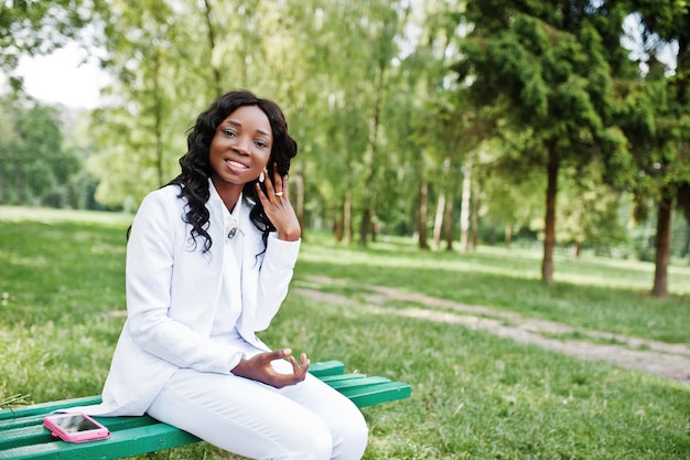 Ritratto ravvicinato di una ragazza afroamericana nera elegante e bella seduta su una panchina con il telefono cellulare