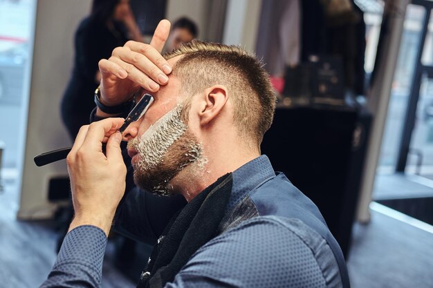 Close-up portrait of a stylish male who himself shaving in a hairdressing salon.