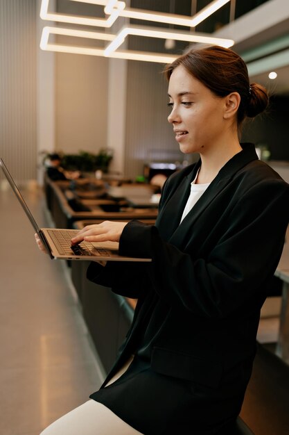 Close up portrait of stylish modern female model is typing on laptop in stylish office