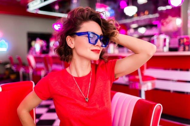 Close-up portrait of stylish smiling woman in colorful outfit in retro vintage 50's cafe sitting at table