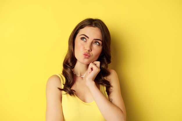 Close up portrait of stylish young beautiful woman thinking yearning smth looking up and making choi...