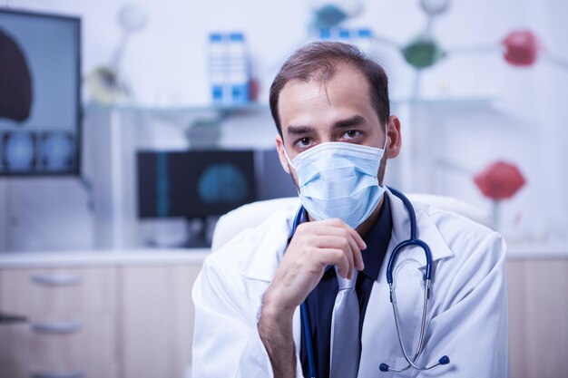 외과 의사 남자 착용 외과 마스크의 초상화를 닫습니다. 클리닉에서 그의 캐비닛에 있는 심각한 젊은 의사.