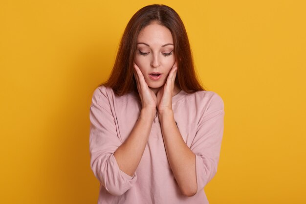 Close up portrait of surprised beautiful girl holding her hands near cheeks and keeps mouth opened