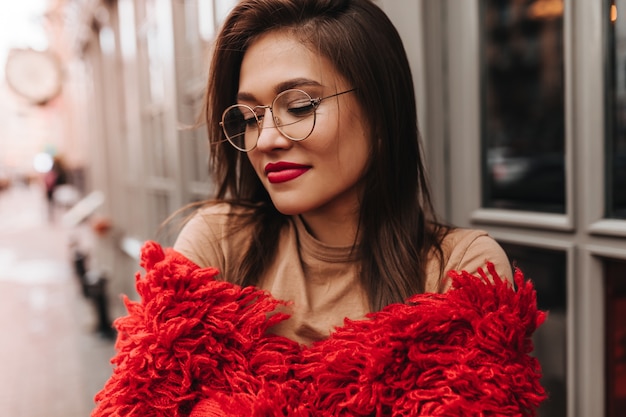 Free photo close-up portrait of tanned dark-haired woman with red lips in glasses against background of beautiful street.