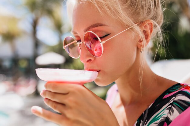 目を閉じてカクテルを飲む日焼けした女性のクローズアップの肖像画。